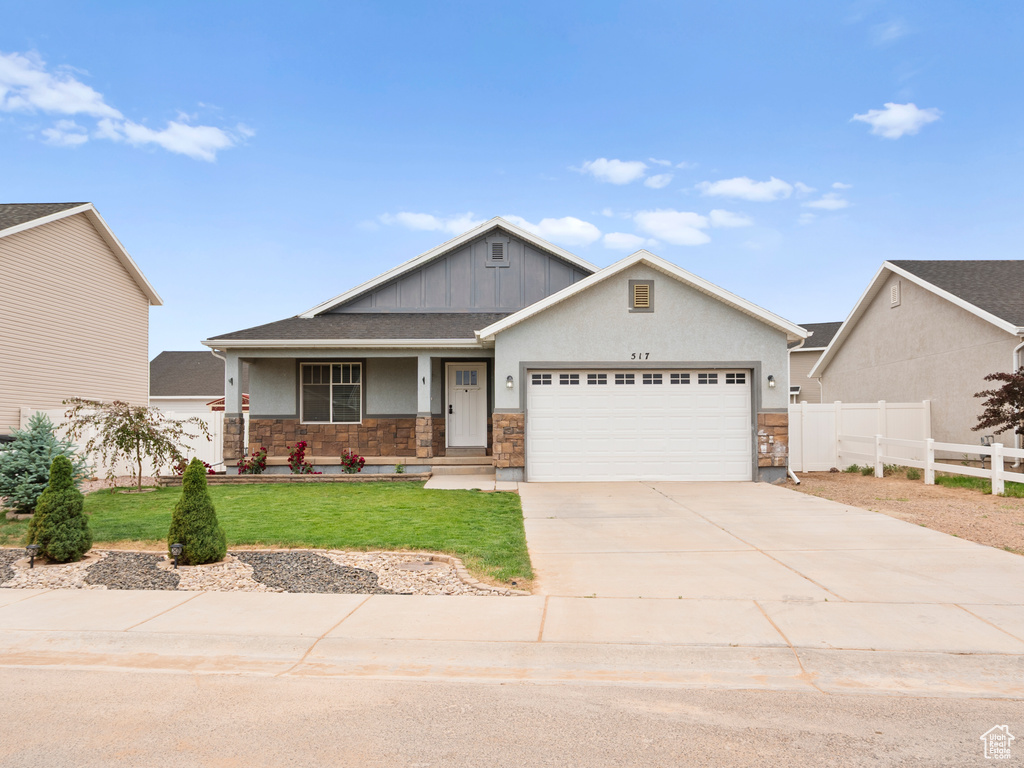 Craftsman-style home featuring an attached garage, stone siding, driveway, covered porch, and board and batten siding