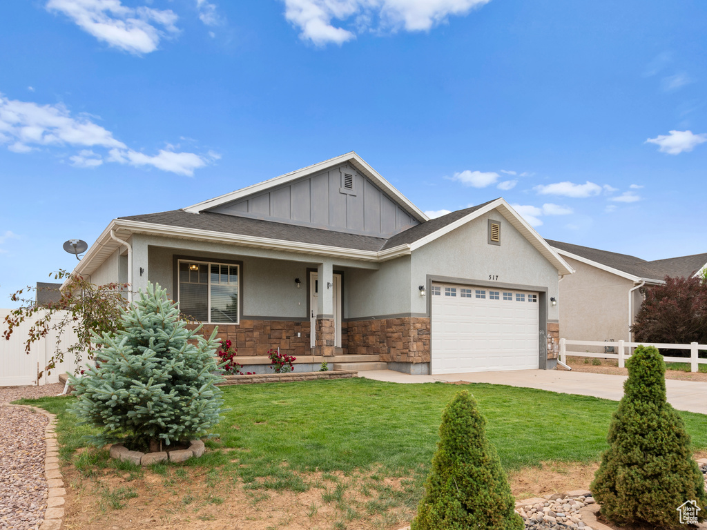 View of front of property featuring stone siding, a garage, a porch, driveway, and board and batten siding