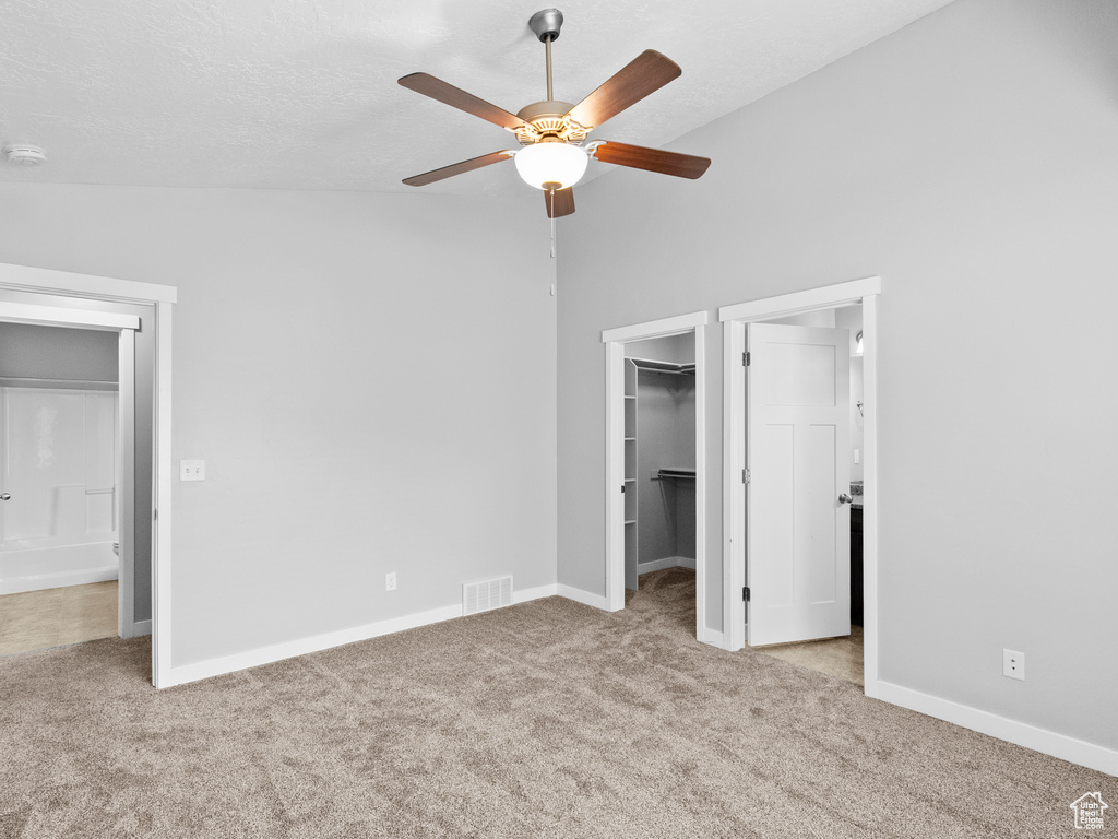 Unfurnished bedroom with carpet floors, a spacious closet, vaulted ceiling, a closet, and ceiling fan