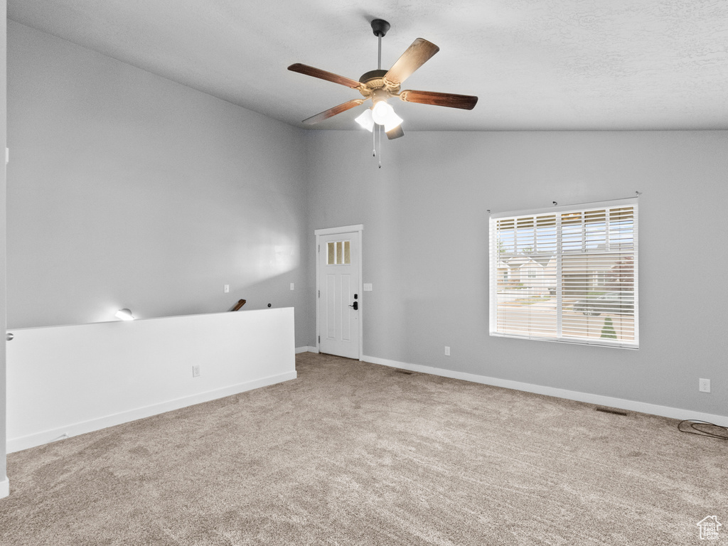 Carpeted empty room with a ceiling fan and vaulted ceiling