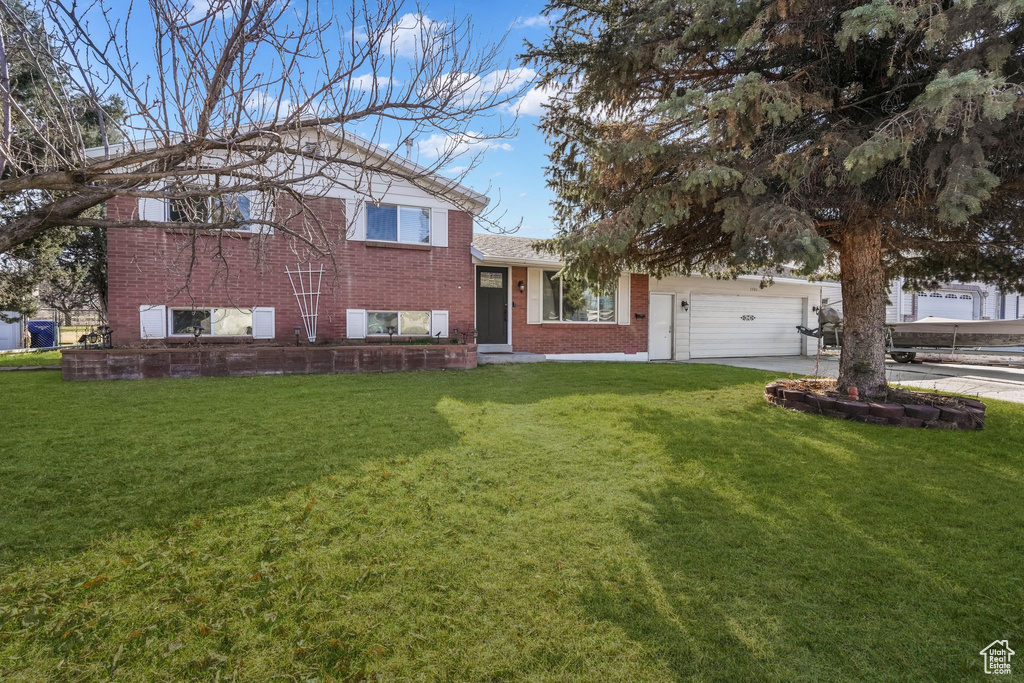 Tri-level home with brick siding, a garage, a front yard, and concrete driveway