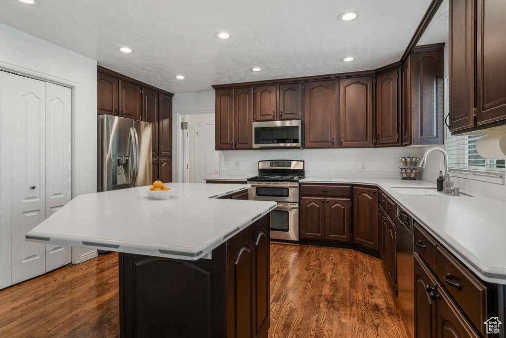 Kitchen featuring stainless steel appliances, a center island, dark brown cabinets, light countertops, and dark wood finished floors