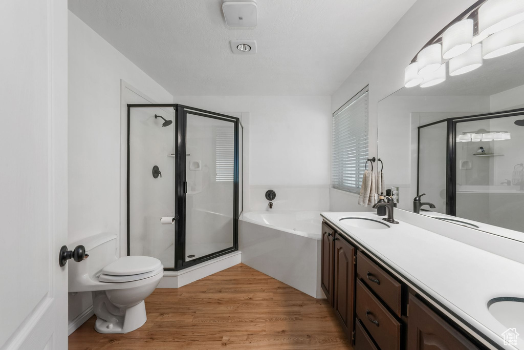 Full bathroom with a stall shower, a garden tub, double vanity, and wood finished floors