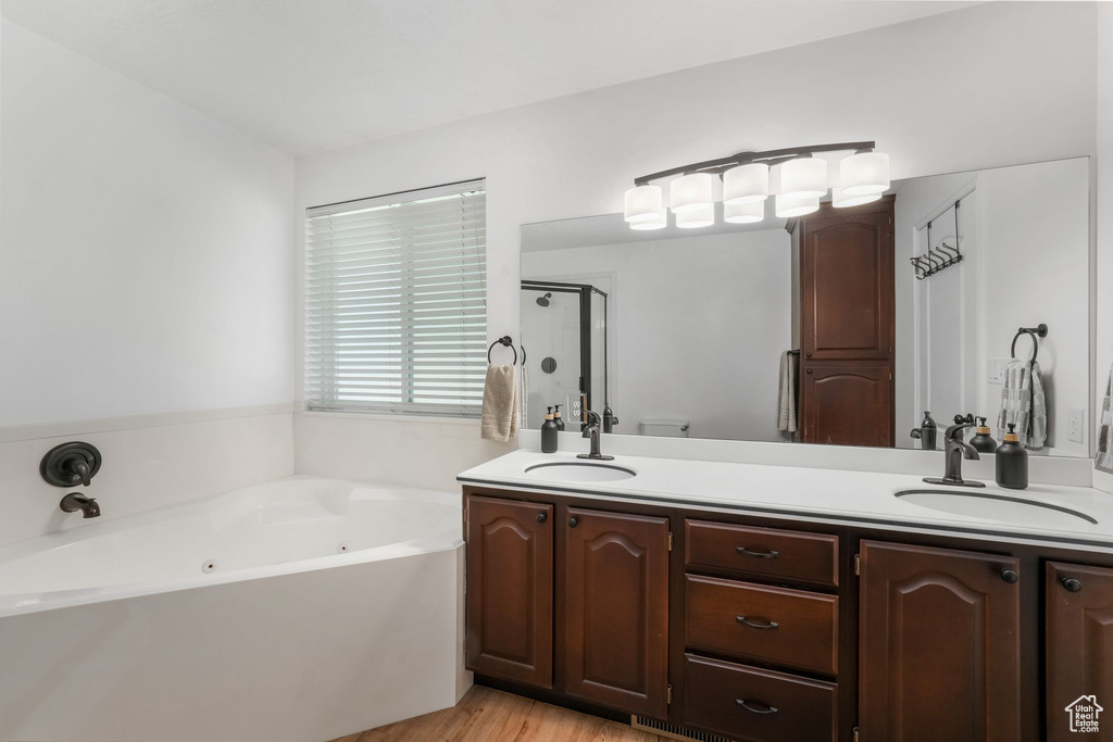Bathroom featuring double vanity, a whirlpool tub, a stall shower, and wood finished floors