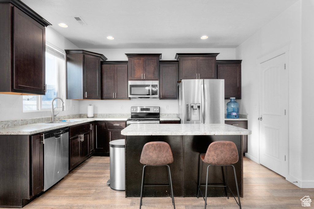 Kitchen with appliances with stainless steel finishes, dark brown cabinetry, a center island, light wood finished floors, and recessed lighting