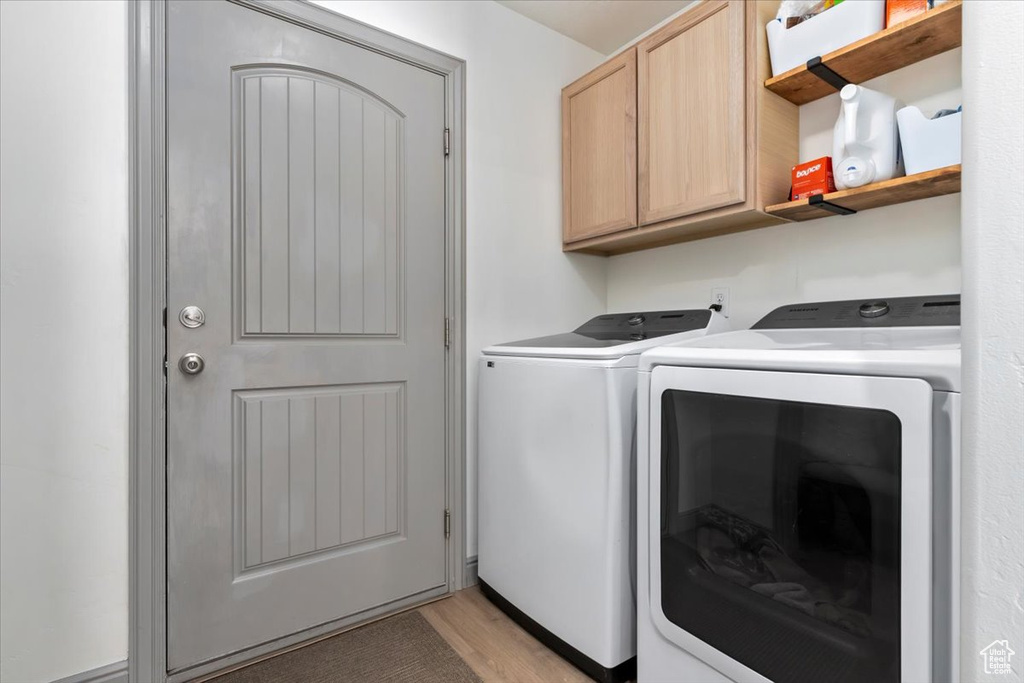 Washroom with cabinet space, washing machine and clothes dryer, and light wood finished floors