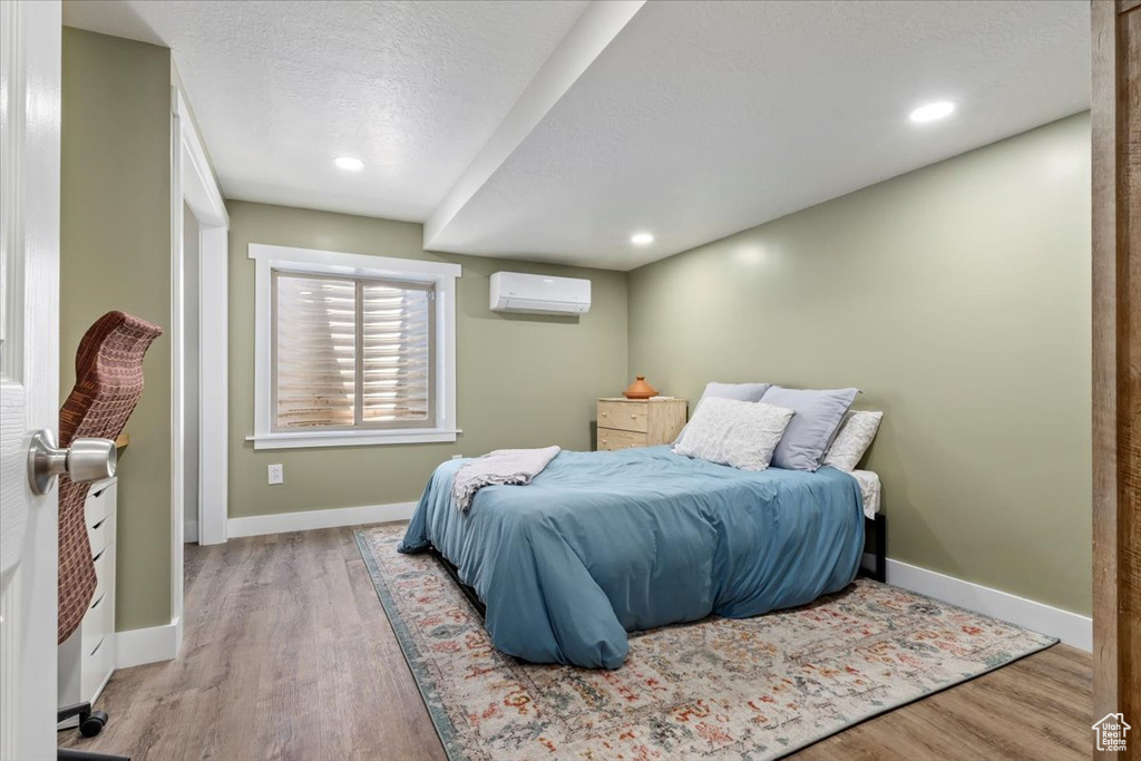 Bedroom with an AC wall unit, wood finished floors, a textured ceiling, and recessed lighting