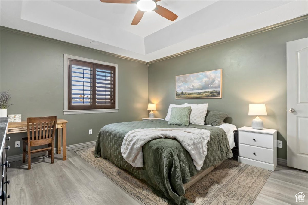 Bedroom with a raised ceiling, light wood-style flooring, and ceiling fan