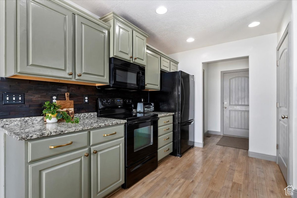 Kitchen featuring black appliances, backsplash, light wood-style flooring, light stone countertops, and gray cabinets