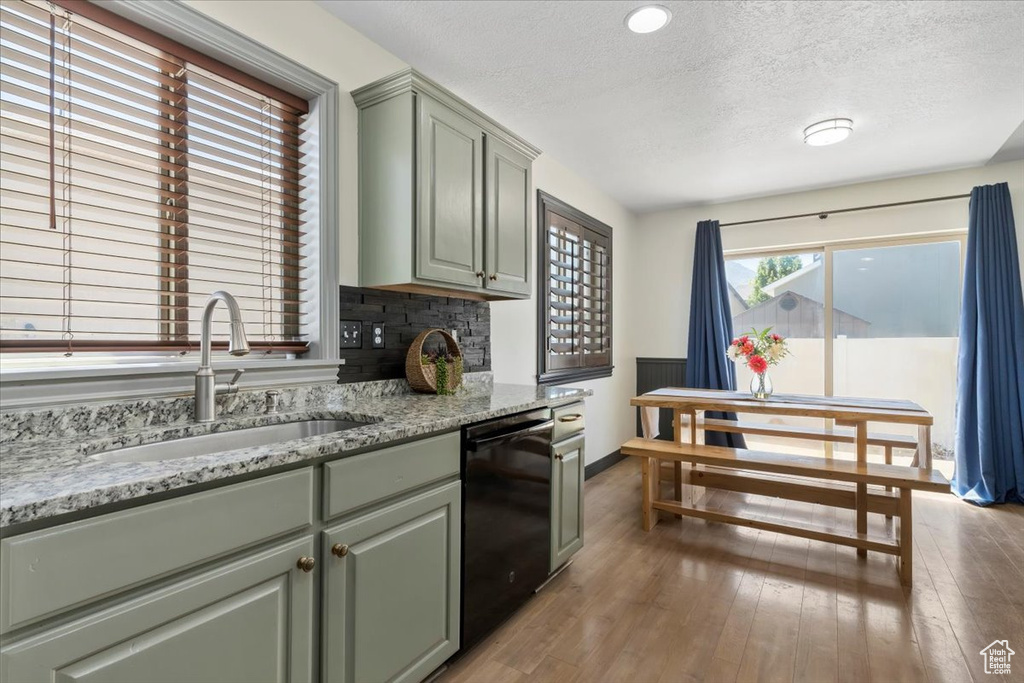 Kitchen featuring dishwasher, a textured ceiling, light wood-type flooring, light stone countertops, and green cabinets
