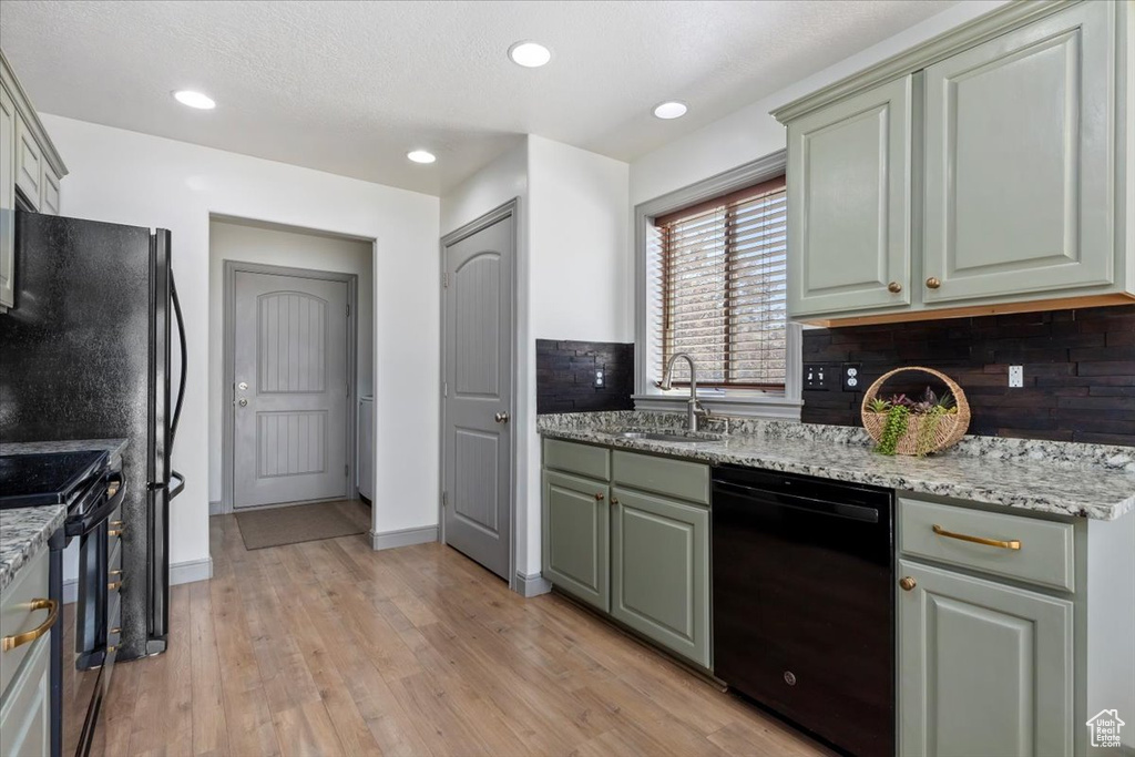 Kitchen with black appliances, light wood-type flooring, light stone counters, recessed lighting, and green cabinets
