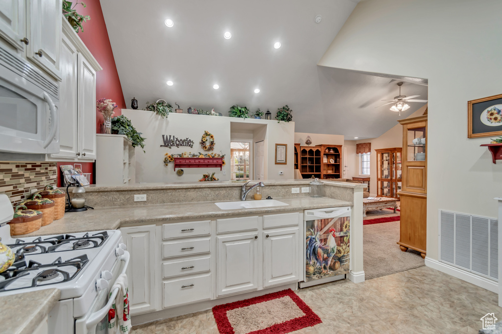Kitchen featuring white appliances, vaulted ceiling, plenty of natural light, light countertops, and a peninsula