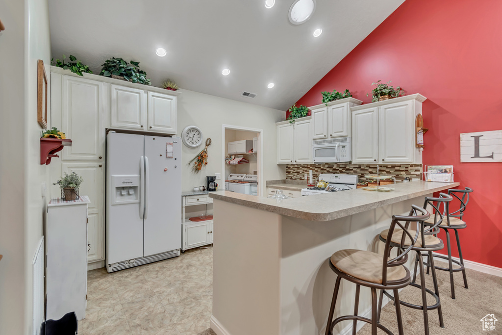 Kitchen featuring white appliances, a peninsula, tasteful backsplash, white cabinetry, and light countertops