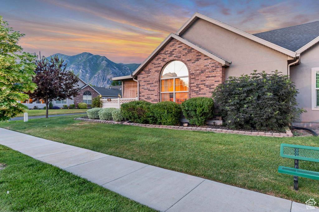 View of front facade featuring a mountain view, a front yard, brick siding, and stucco siding