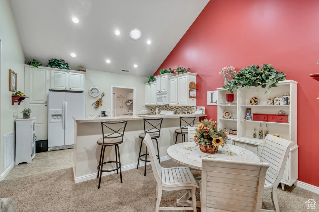 Dining room with high vaulted ceiling, light carpet, and recessed lighting