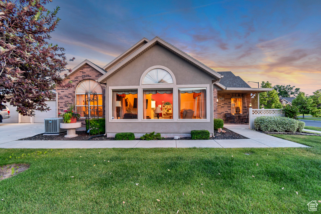 Back of house at dusk with a yard, brick siding, and stucco siding