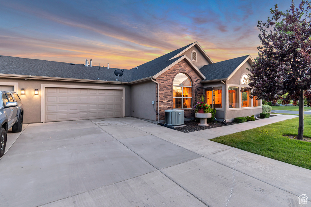 Ranch-style home with a garage, concrete driveway, stucco siding, roof with shingles, and a yard