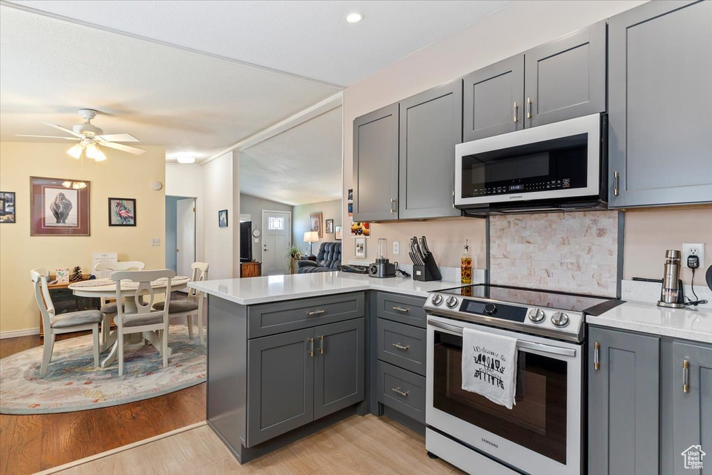 Kitchen featuring stainless steel electric range, gray cabinetry, a peninsula, light wood finished floors, and light countertops