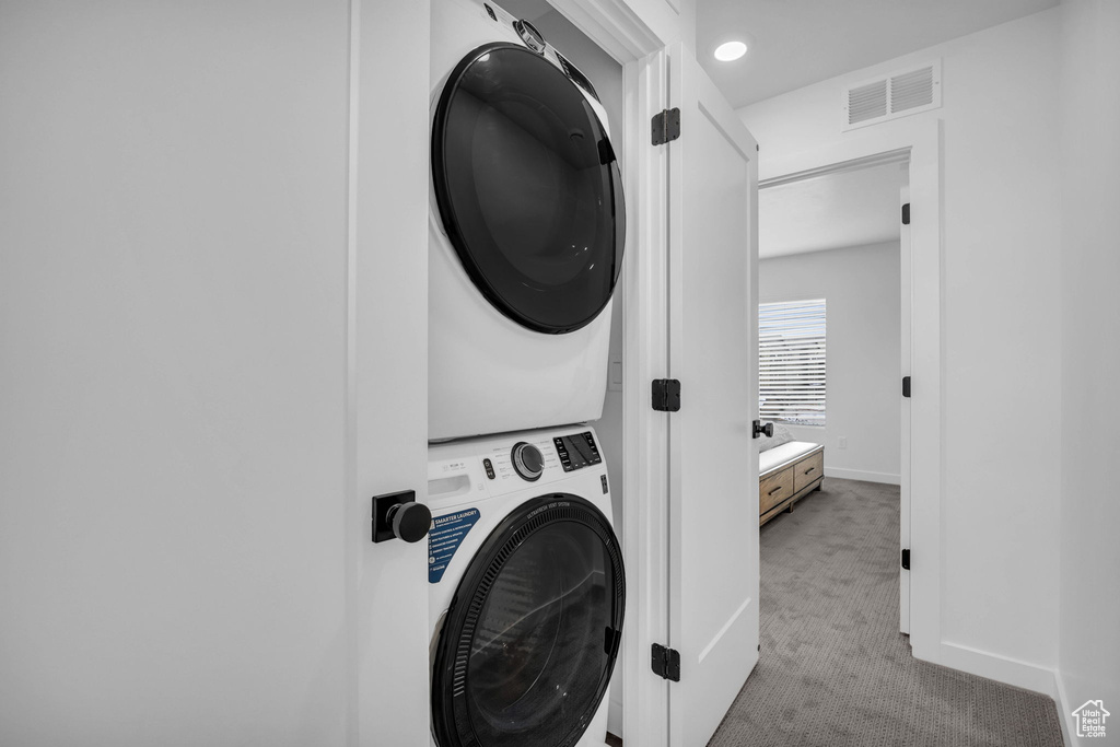 Laundry room with stacked washing machine and dryer and carpet