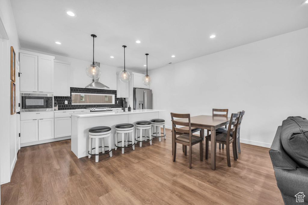 Kitchen with appliances with stainless steel finishes, a breakfast bar, backsplash, white cabinetry, and wood finished floors