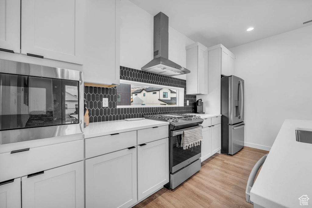 Kitchen featuring appliances with stainless steel finishes, wall chimney exhaust hood, tasteful backsplash, light countertops, and recessed lighting