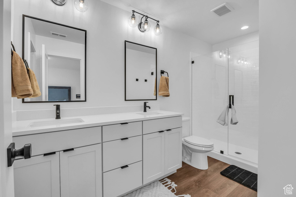 Bathroom featuring a stall shower, wood finished floors, double vanity, and recessed lighting
