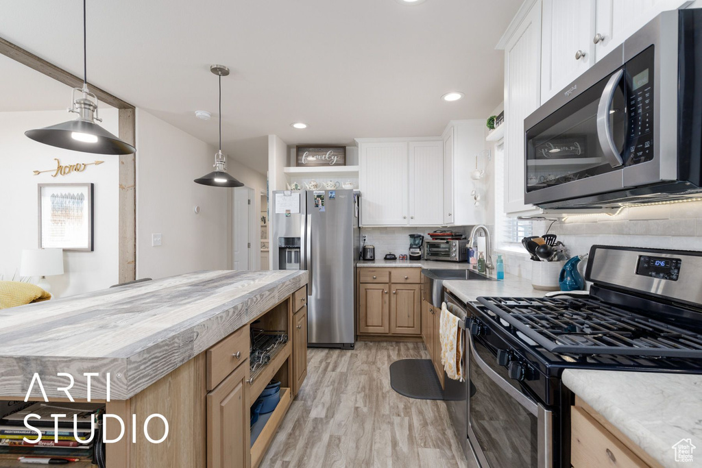 Kitchen featuring appliances with stainless steel finishes, open shelves, light countertops, tasteful backsplash, and light wood finished floors