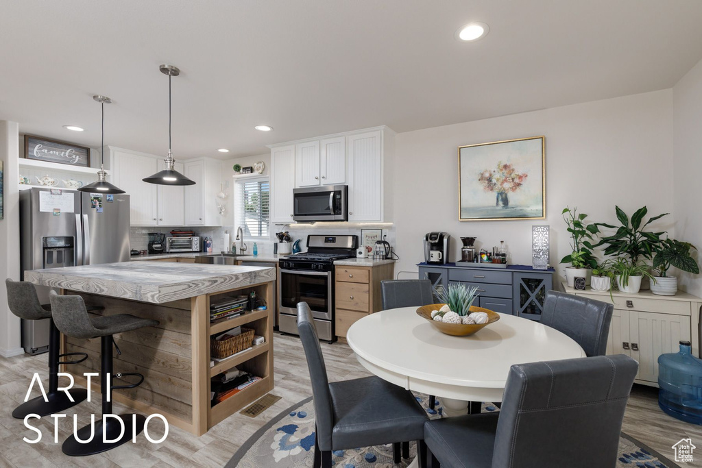 Kitchen featuring stainless steel appliances, open shelves, a breakfast bar area, white cabinets, and light stone countertops
