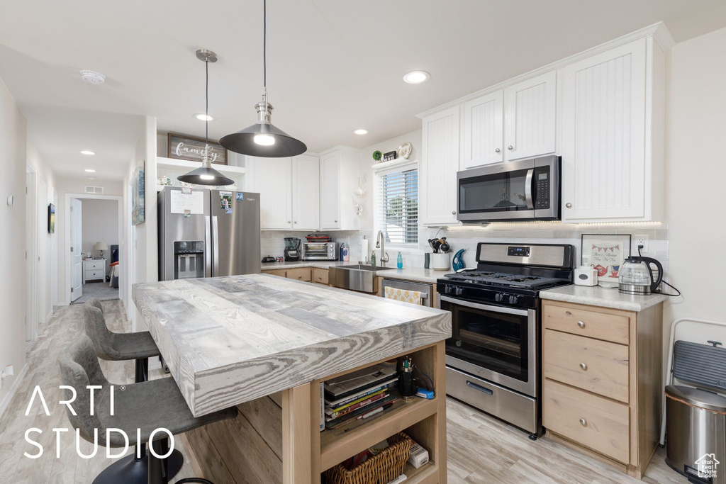 Kitchen with stainless steel appliances, light countertops, light wood finished floors, hanging light fixtures, and white cabinets