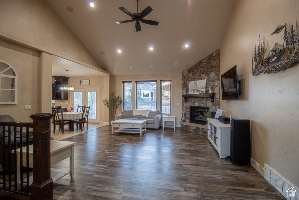 Living room with high vaulted ceiling, dark wood-style floors, ceiling fan, a stone fireplace, and recessed lighting