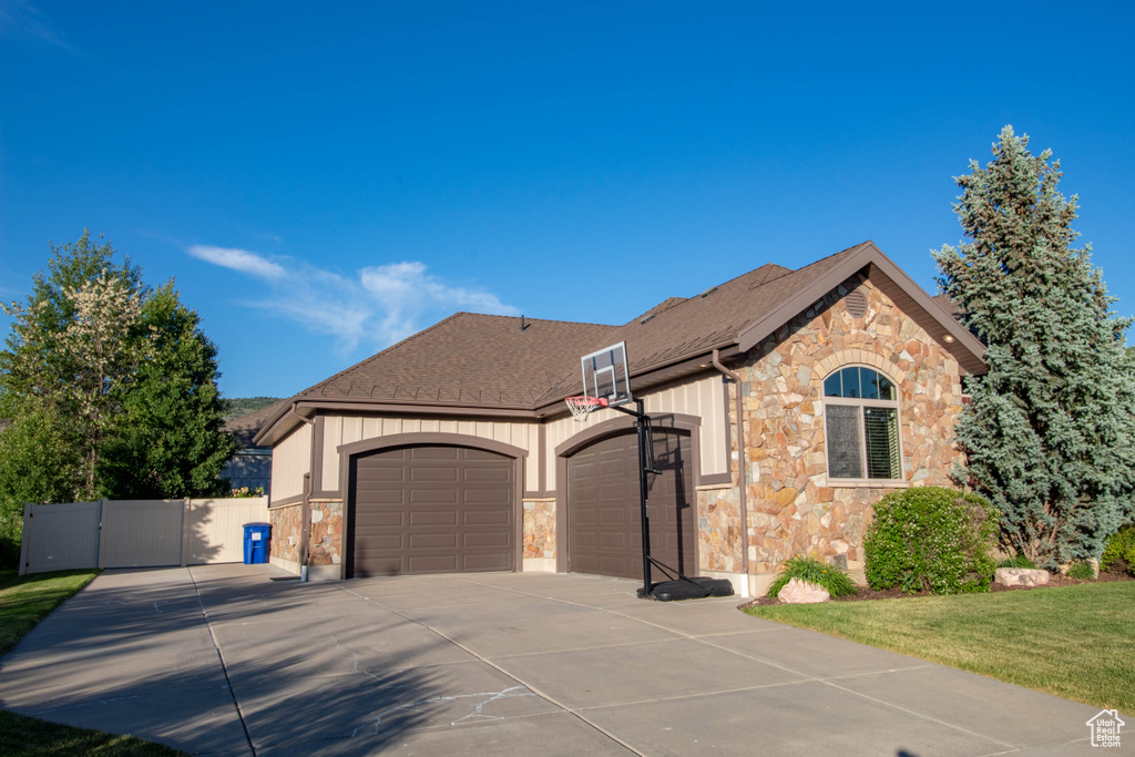 View of front facade featuring stone siding, an attached garage, concrete driveway, a gate, and a shingled roof