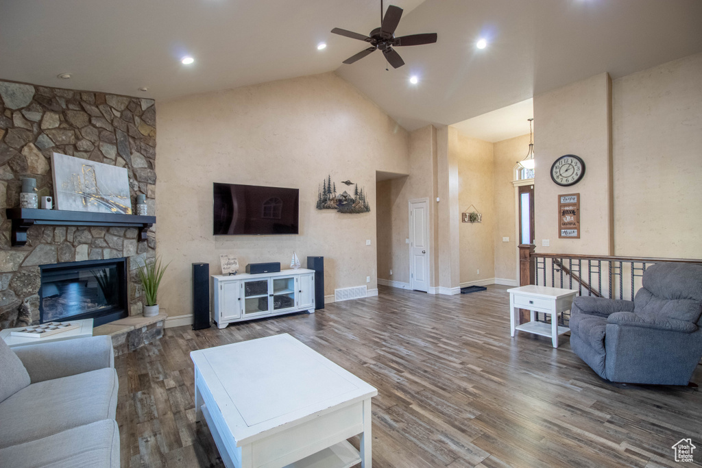 Living area with high vaulted ceiling, a ceiling fan, wood finished floors, and a stone fireplace