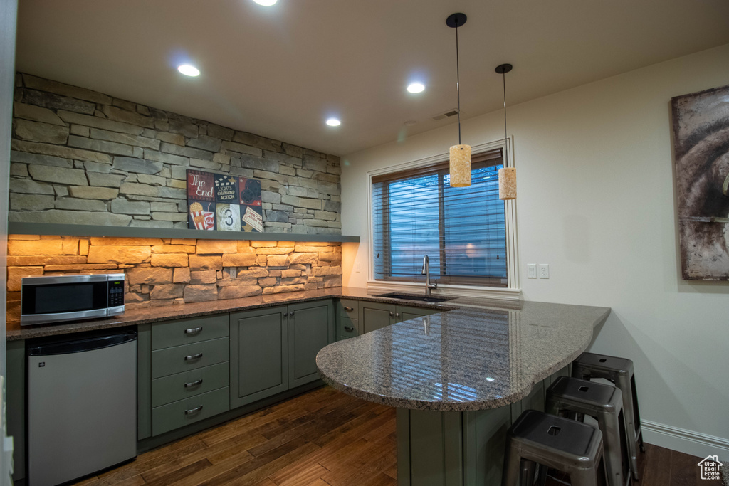 Kitchen with refrigerator, stainless steel microwave, a peninsula, dark wood-type flooring, and a kitchen breakfast bar