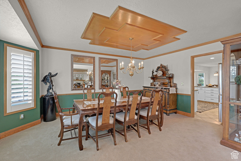Dining area featuring light carpet, a textured ceiling, ornamental molding, and a chandelier