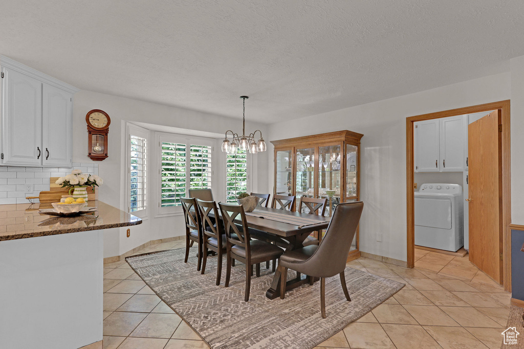 Dining area featuring washer / clothes dryer, light tile patterned floors, a chandelier, and a textured ceiling