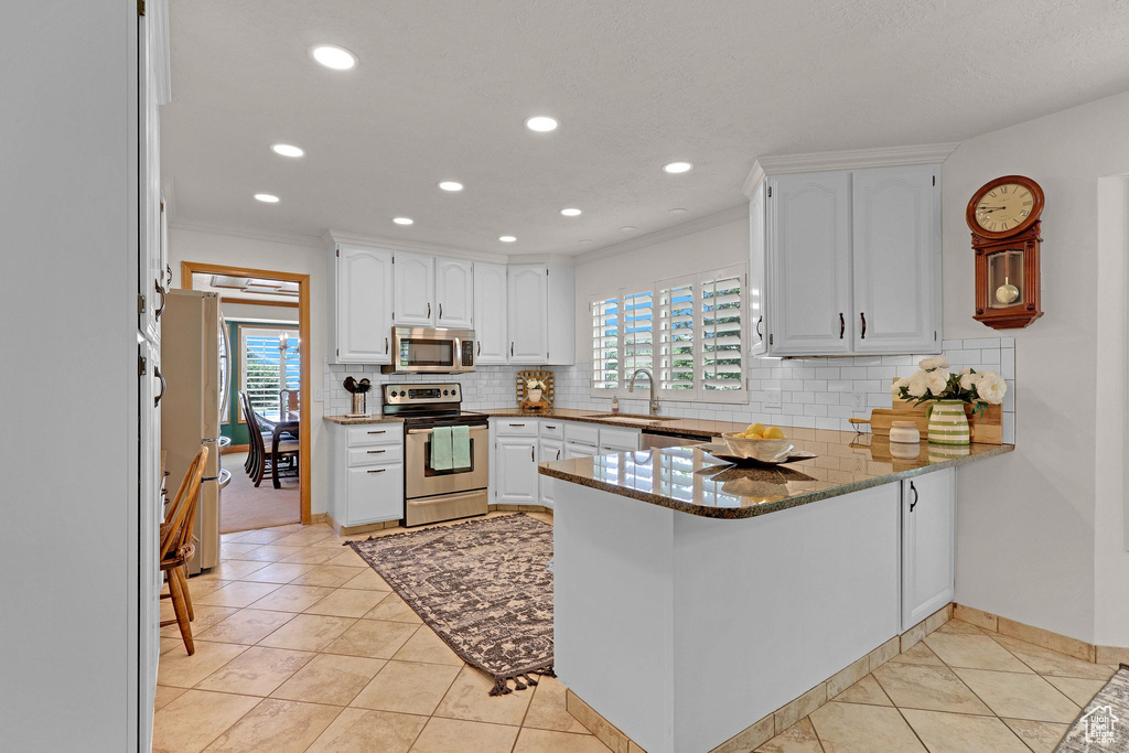 Kitchen with appliances with stainless steel finishes, a peninsula, healthy amount of natural light, white cabinetry, and crown molding