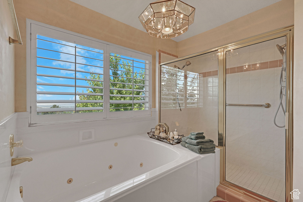 Full bath featuring a tub with jets, a chandelier, and a stall shower