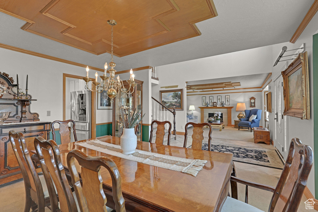 Dining space with a tray ceiling, crown molding, a chandelier, stairs, and light colored carpet