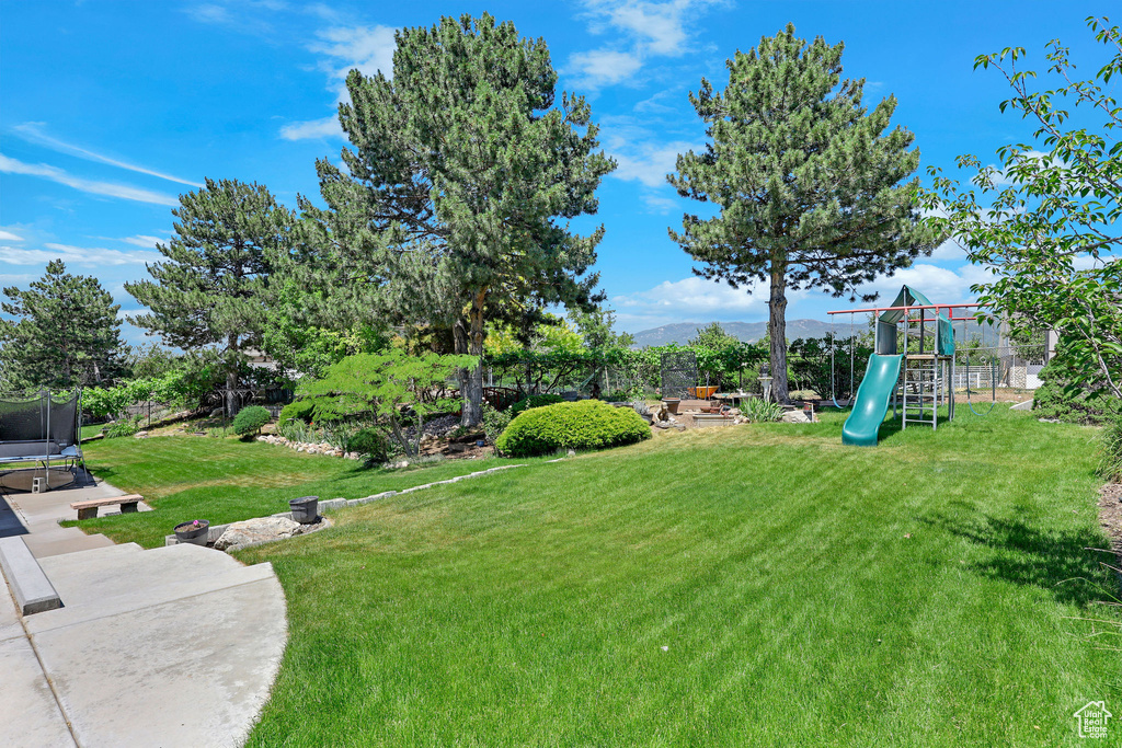 View of grassy yard featuring a trampoline, a playground, and a mountain view