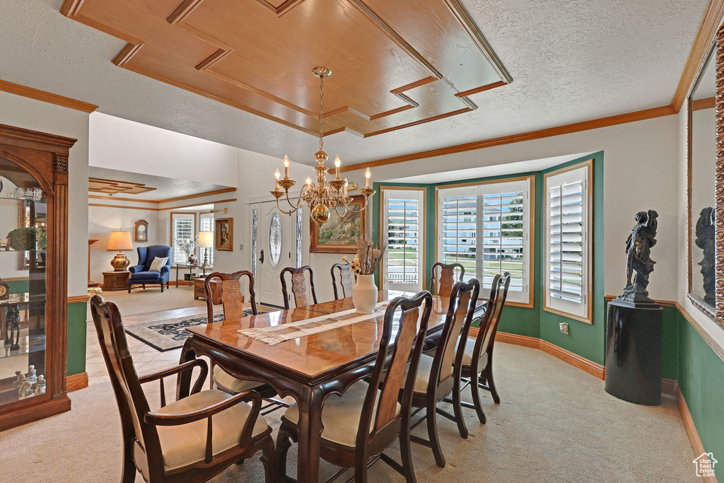 Dining area with light colored carpet, a textured ceiling, a chandelier, and ornamental molding