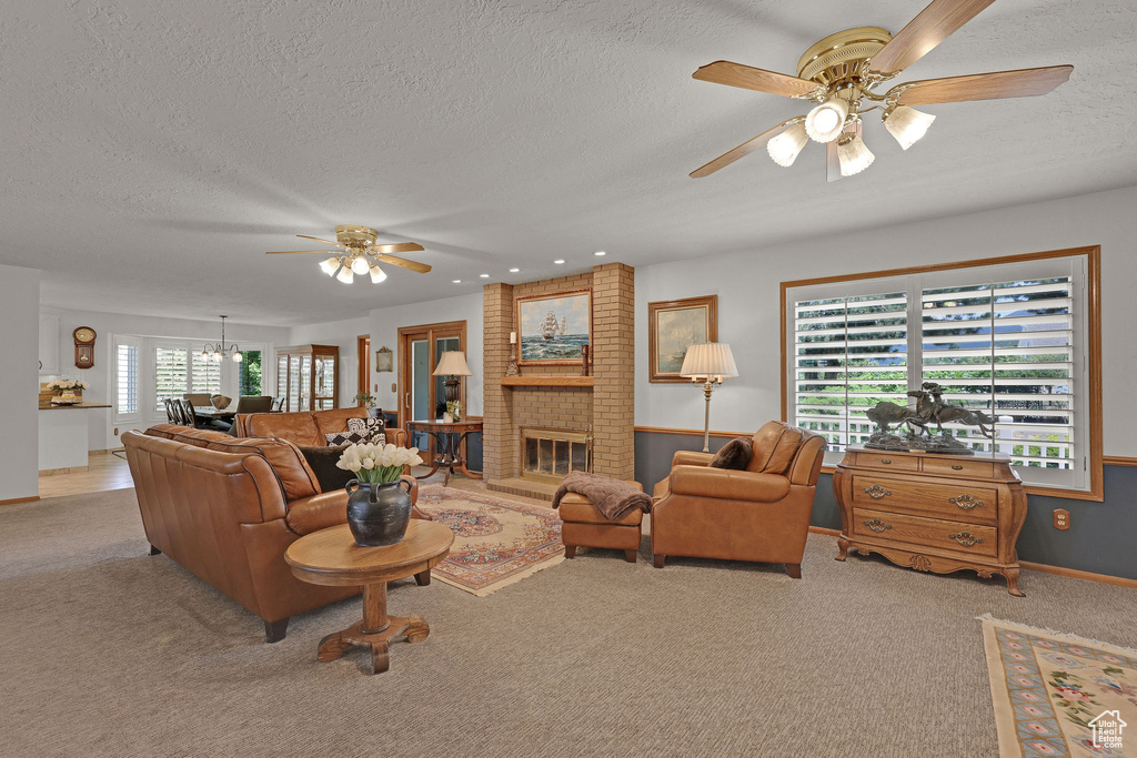 Carpeted living room featuring ceiling fan, a textured ceiling, a brick fireplace, and a chandelier