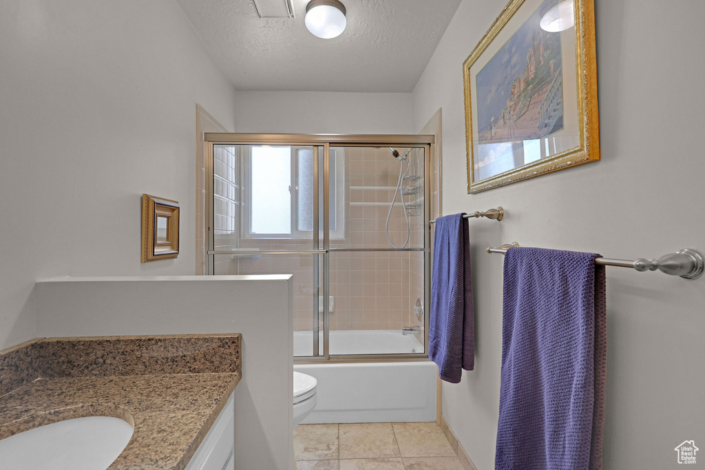Full bath featuring vanity, a textured ceiling, enclosed tub / shower combo, and tile patterned floors