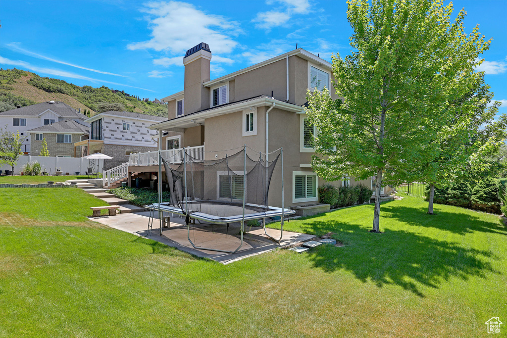 Back of property with stucco siding, a patio area, a trampoline, and a chimney