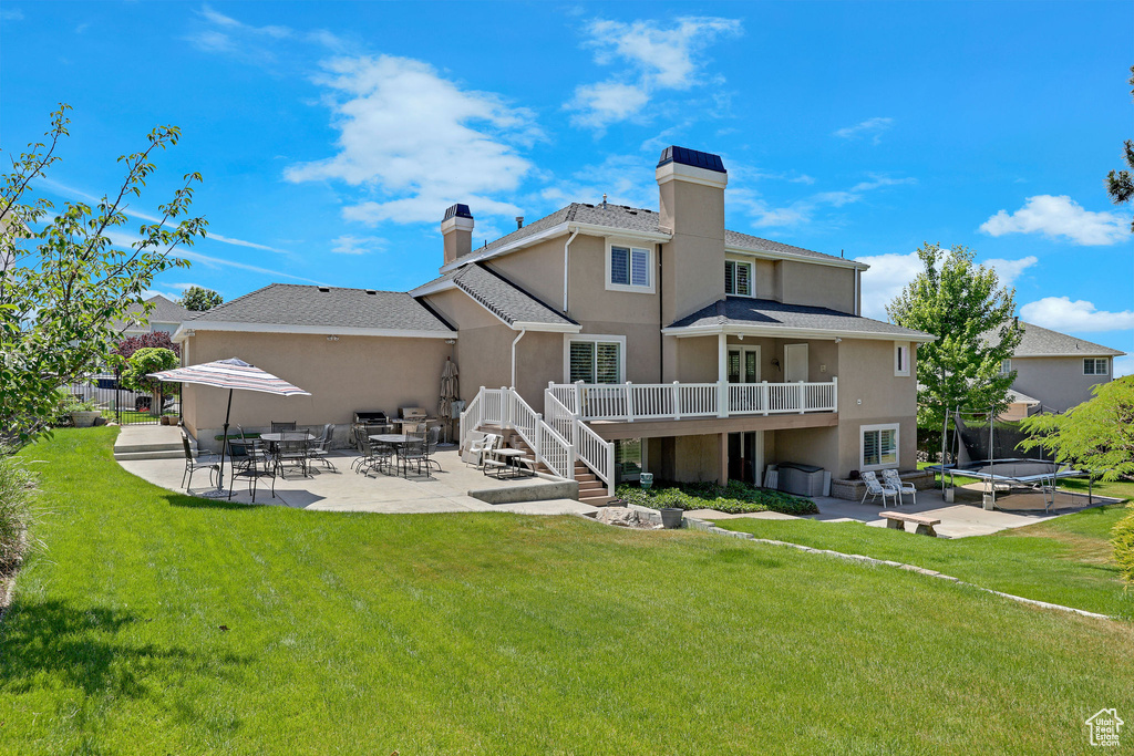 Back of house featuring a chimney, a patio, a trampoline, and stucco siding