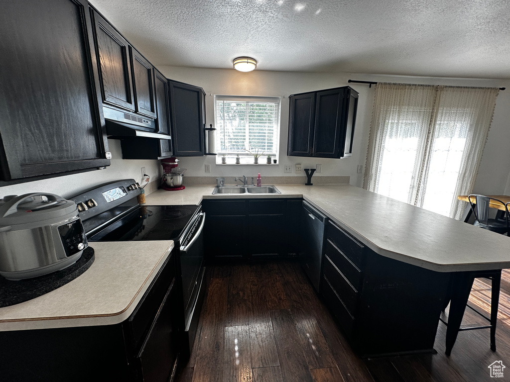 Kitchen featuring electric range oven, a peninsula, dishwasher, under cabinet range hood, and a textured ceiling