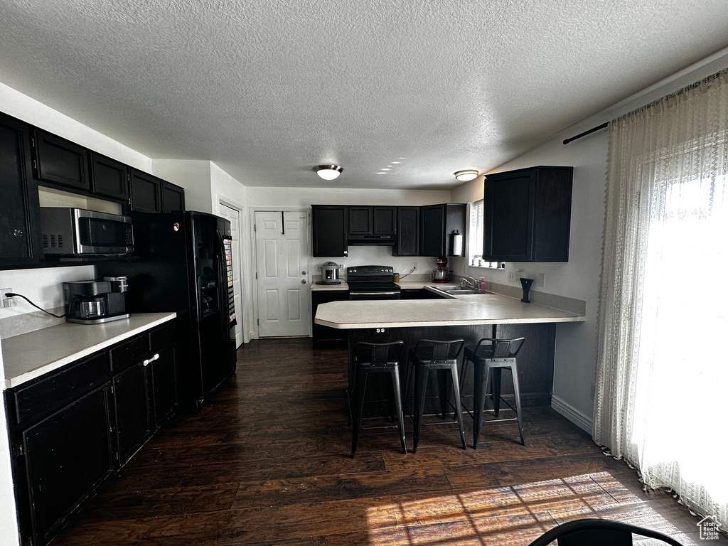 Kitchen with black range with electric cooktop, stainless steel microwave, dark cabinetry, and a textured ceiling