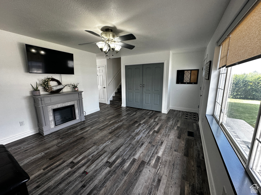 Unfurnished living room featuring dark wood-type flooring, ceiling fan, a textured ceiling, a glass covered fireplace, and stairway