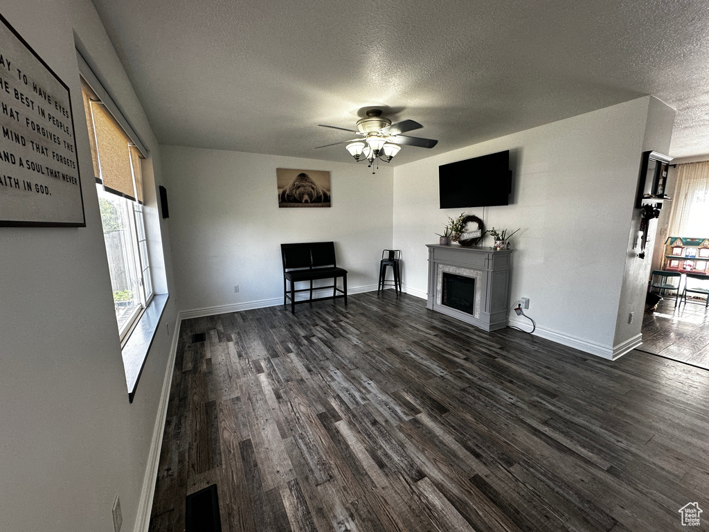 Unfurnished living room with a textured ceiling, dark wood-style flooring, a ceiling fan, and a fireplace
