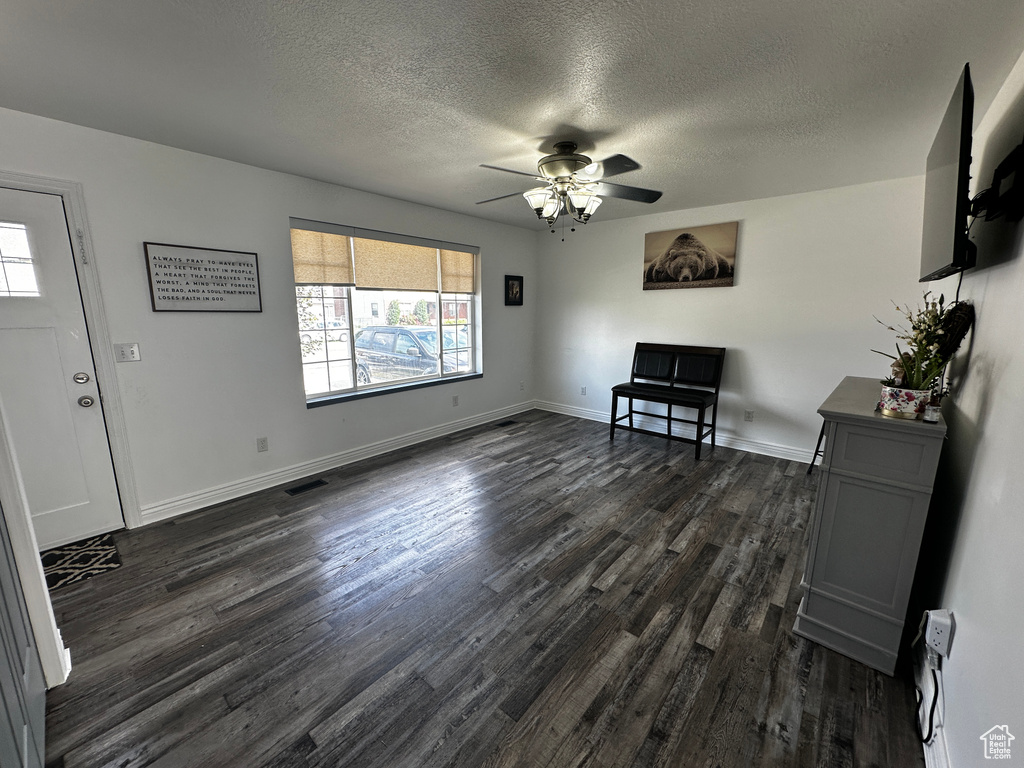 Unfurnished living room featuring dark wood-style floors, a textured ceiling, and a ceiling fan