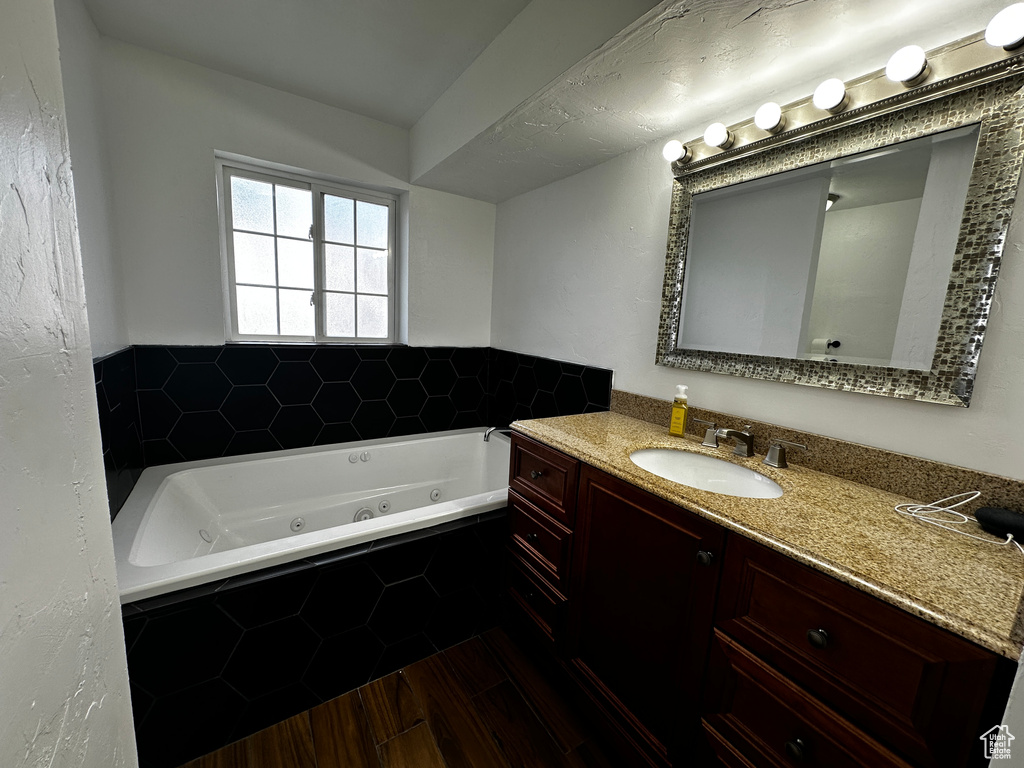 Bathroom with a jetted tub, vanity, and wood finished floors